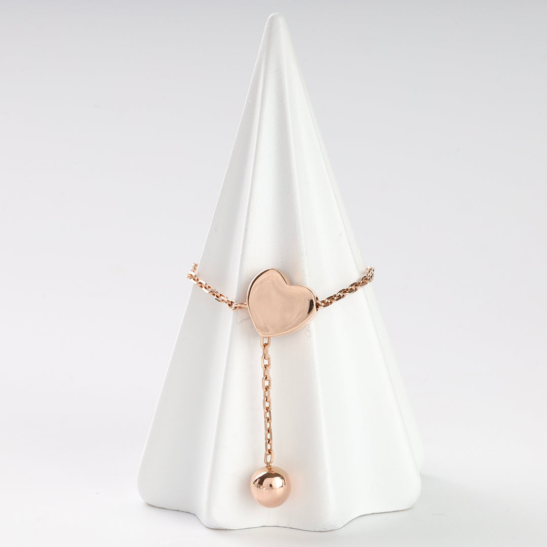 Rose gold heart chain ring with a dangling charm displayed on a white cone stand.