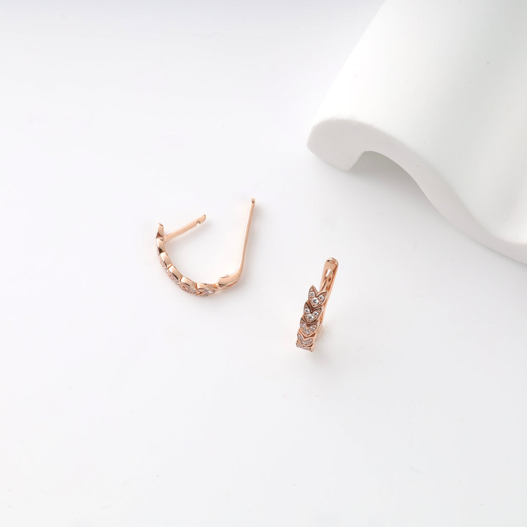 Rose gold huggie earrings with crystal leaf design on a white background.