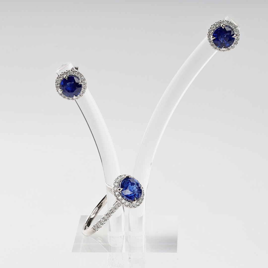 Silver ring and stud earrings with round blue stones and clear accents on a white jewelry display. Sapphire halo jewelry set.