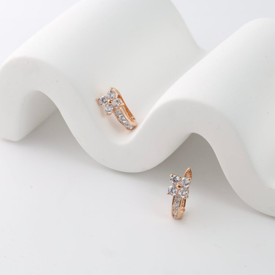 Rose gold hoop earrings with cubic zirconia flower design on white display.