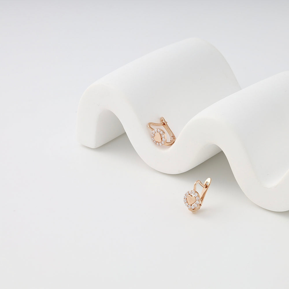 Rose gold kids earrings with small pavé crystals, displayed on a white curved stand.