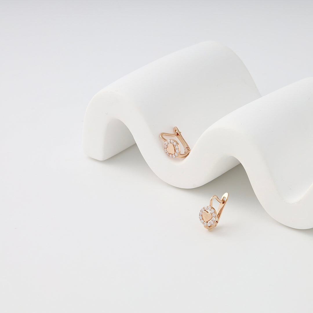 Rose gold kids earrings with small pavé crystals, displayed on a white curved stand.