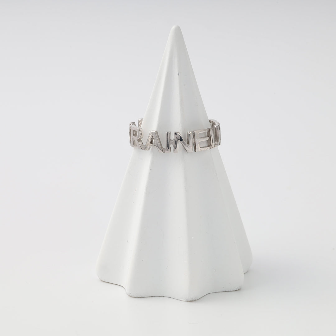 Sterling silver word band ring reading “UKRAINED” on a white display cone, minimalist Ukrainian Jewelry gift ring.