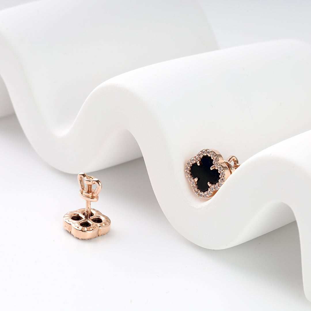 Pair of rose gold stud earrings with black four-leaf clover and clear crystal border on white background.