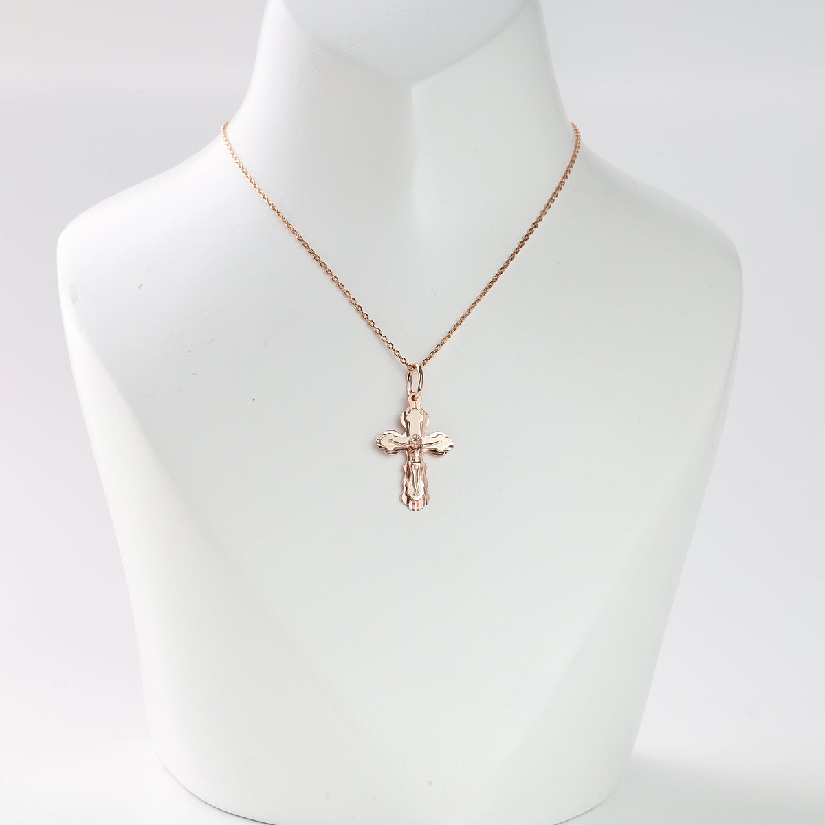 Gold crucifix pendant necklace displayed on a white bust, religious jewelry, cross charm, rose gold chain.