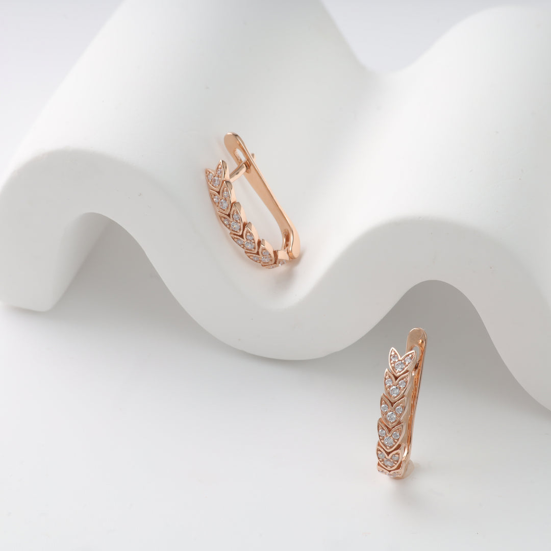 Rose gold leaf earrings with crystal accents on a white wave display.