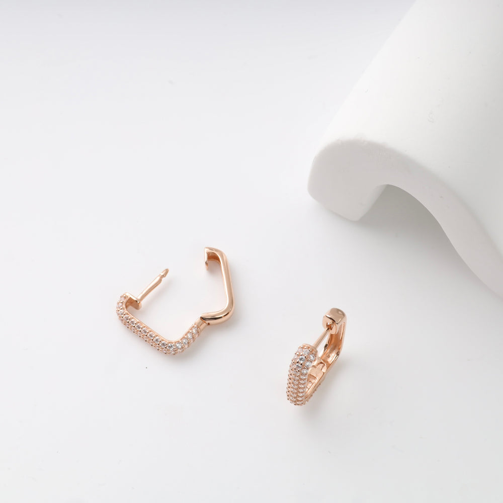 Rose gold hoop earrings with pavé crystals on a white surface.