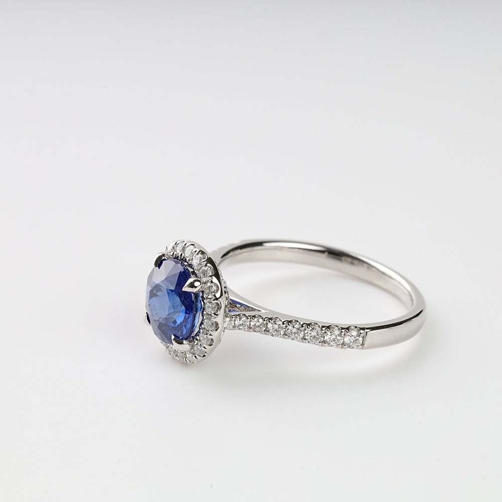 Silver ring with a round blue gemstone center and small clear stones set along the band on a white background.