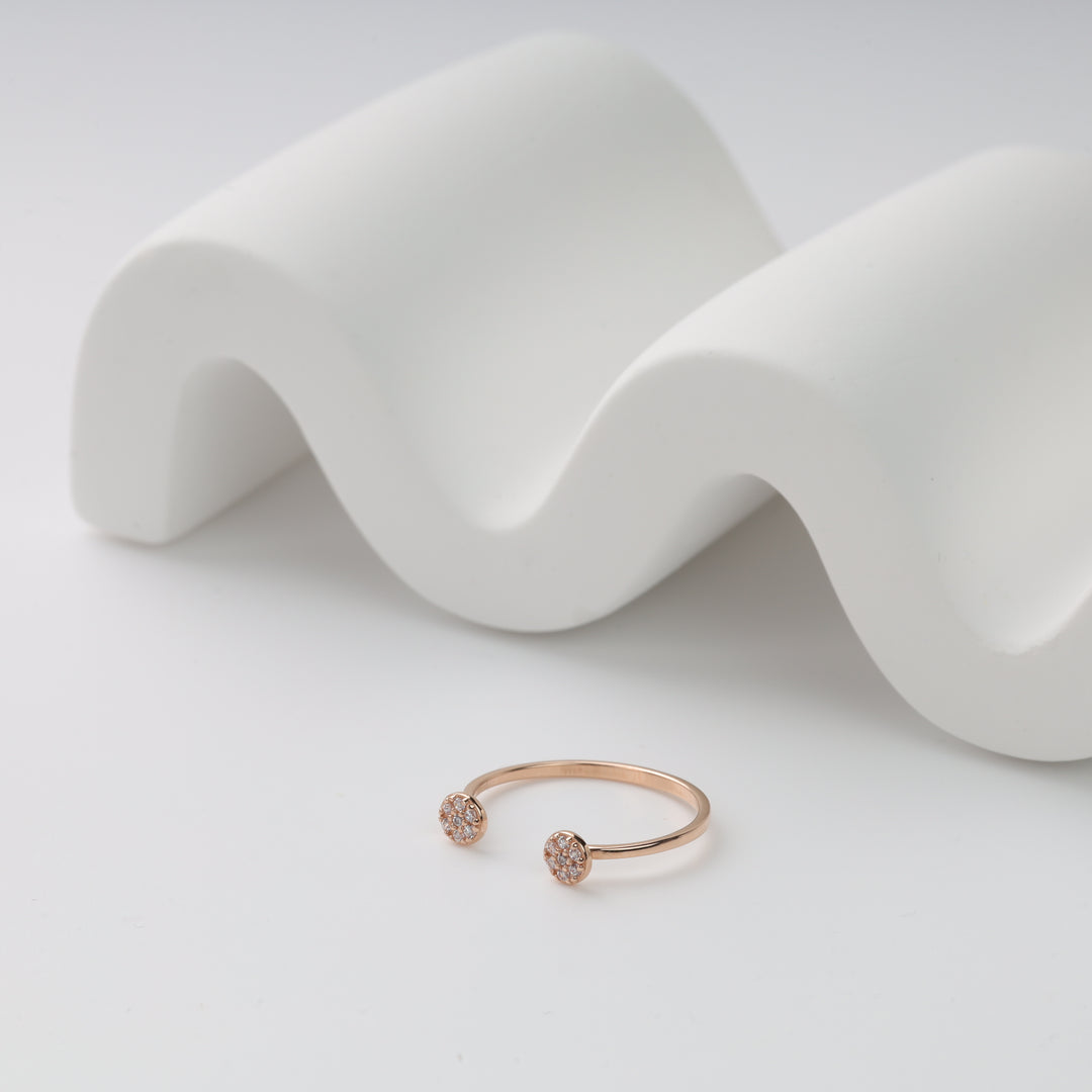 Gold open ring with two circle diamond accents on a white wave stand.