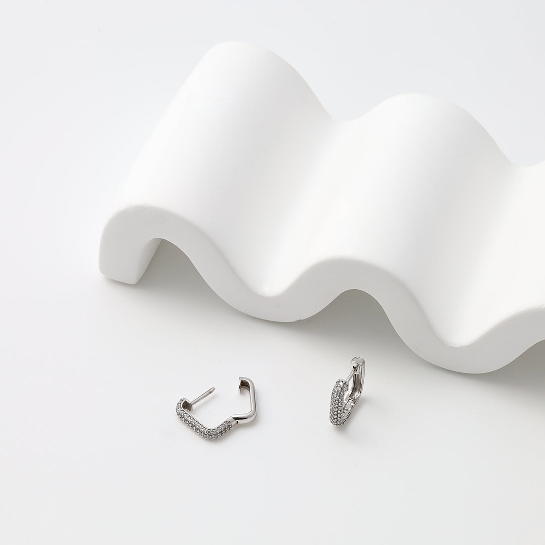 Sterling silver geometric hoop earrings with pavé stones on a white display, Ukrainian Jewelry, modern silver hoop earrings.