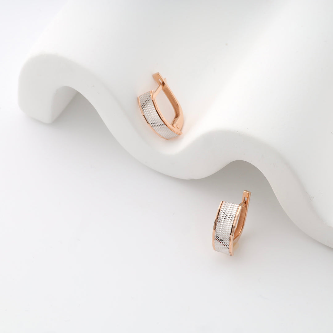 Rose gold and silver hoop earrings on a white wavy stand.
