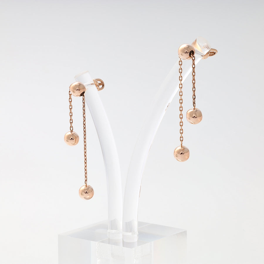 Pair of rose gold dangle earrings with three polished ball charms on delicate chains, displayed on a white stand.