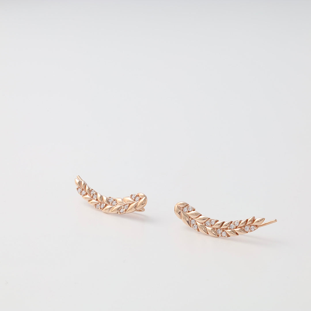Pair of gold leaf climber earrings with small clear crystals displayed on a white background, minimalist jewelry, leaf earrings.
