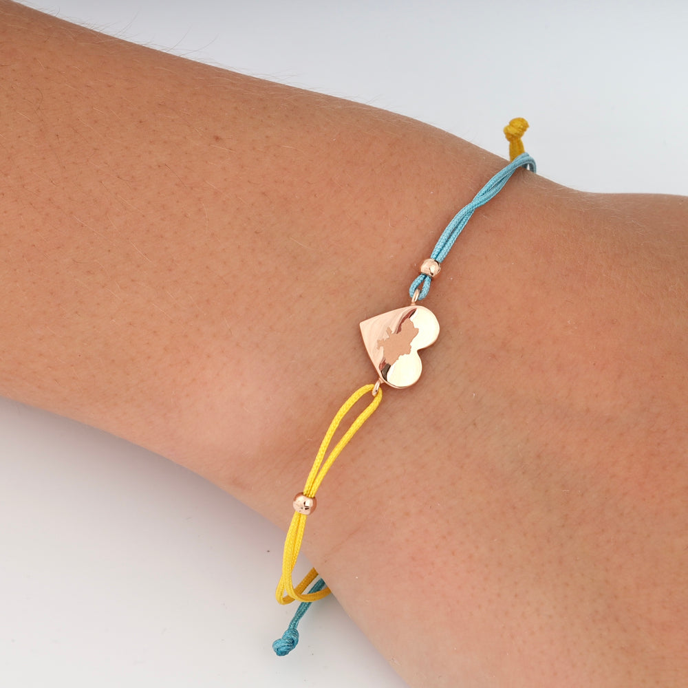 Heart charm bracelet with yellow and blue cords on wrist. Rose gold heart pendant, adjustable.