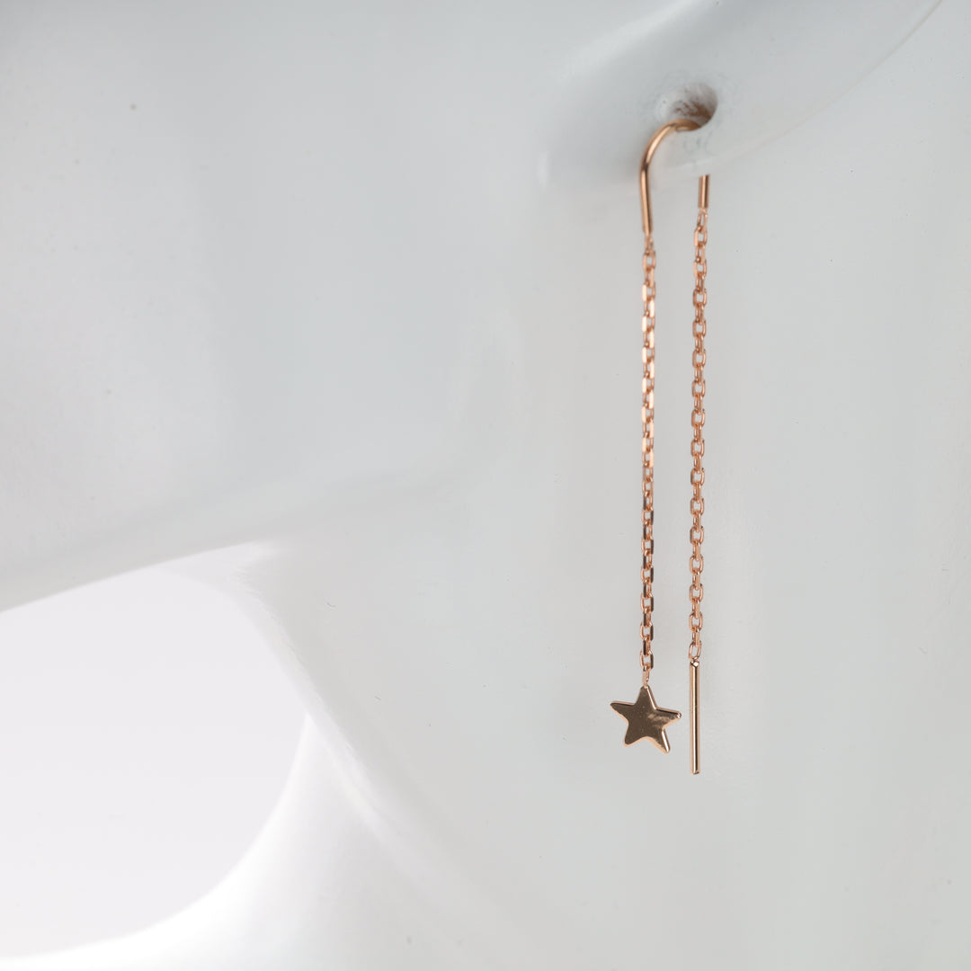 Rose gold chain earrings with a star charm displayed on an ear mannequin.
