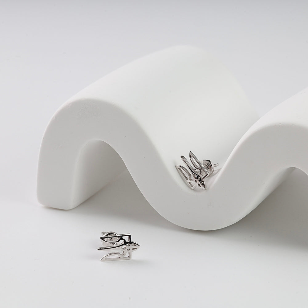 Pair of silver stud earrings with an abstract geometric design, displayed on a curved white ceramic stand.
