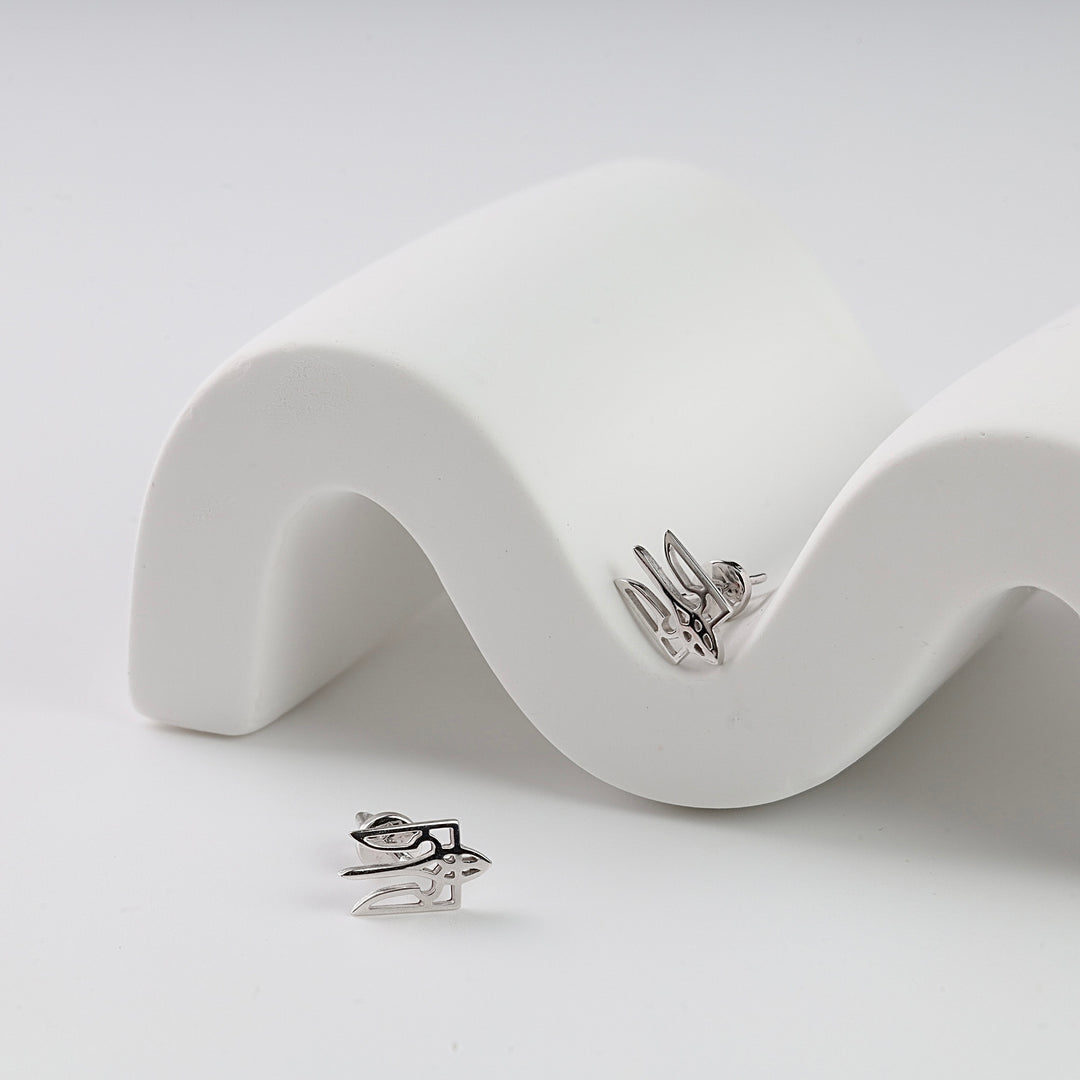 Pair of silver stud earrings with an abstract geometric design, displayed on a curved white ceramic stand.
