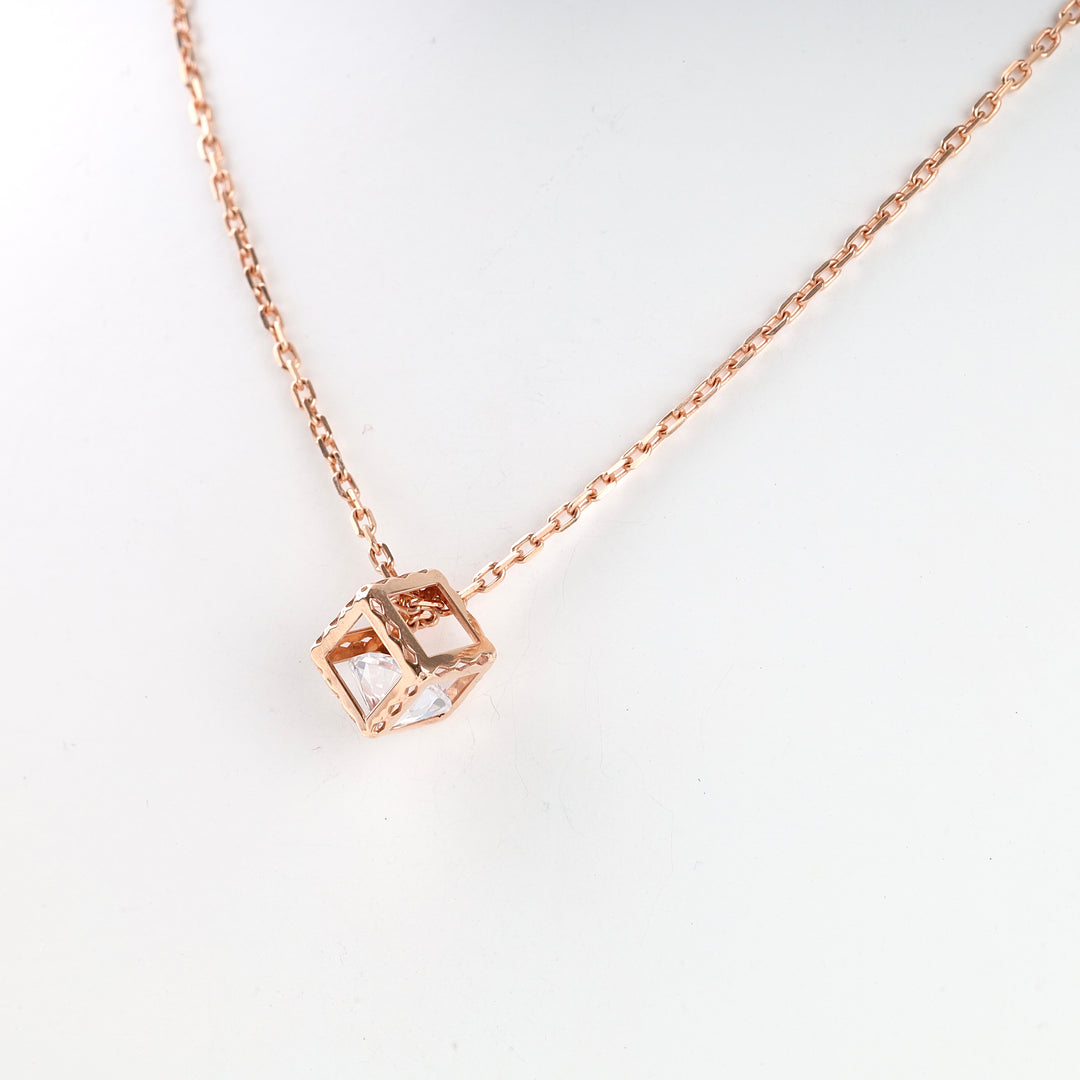 Rose gold chain necklace with a geometric open cube pendant and clear crystal, displayed on a plain white background.