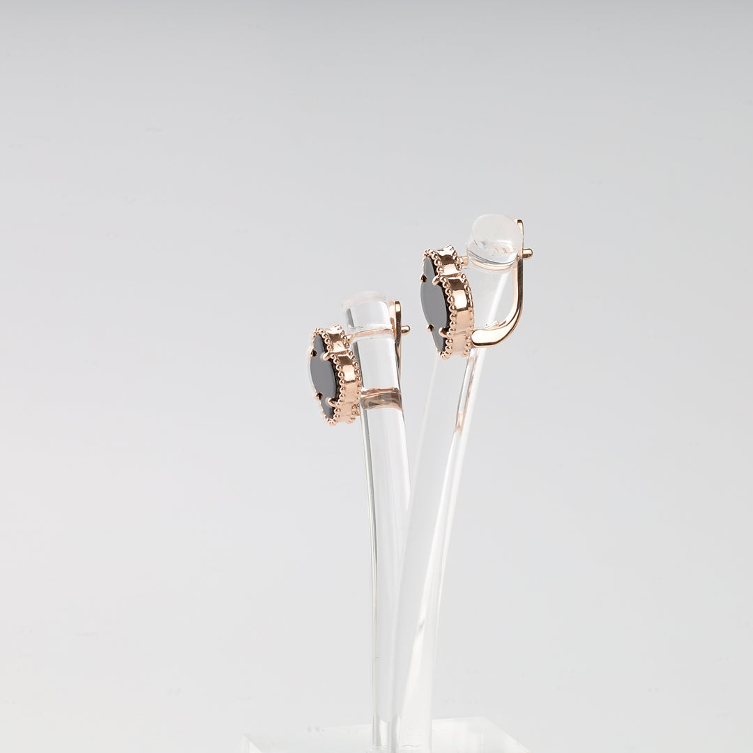 Pair of rose gold oval earrings with black stones and beaded edges displayed on a clear acrylic stand.
