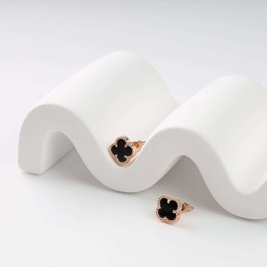 Pair of rose gold clover stud earrings with black enamel on white display.