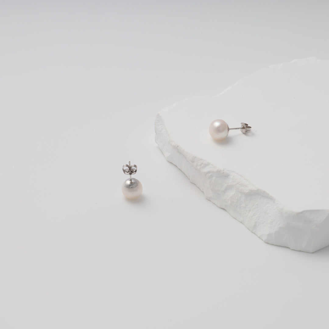 Sterling silver pearl stud earrings on white stone display, classic Ukrainian Jewelry for minimalist silver earrings shoppers.