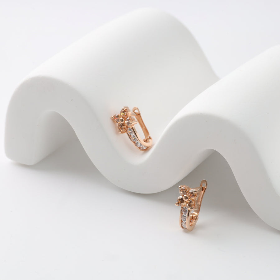 Rose gold floral hoop earrings with crystal accents on white wavy display.
