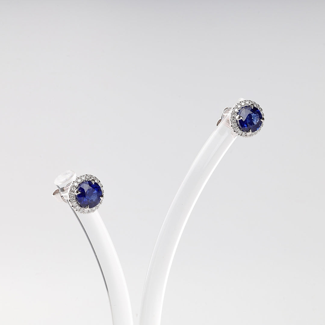 Silver stud earrings with round blue stones and small clear crystals, displayed on a white holder.