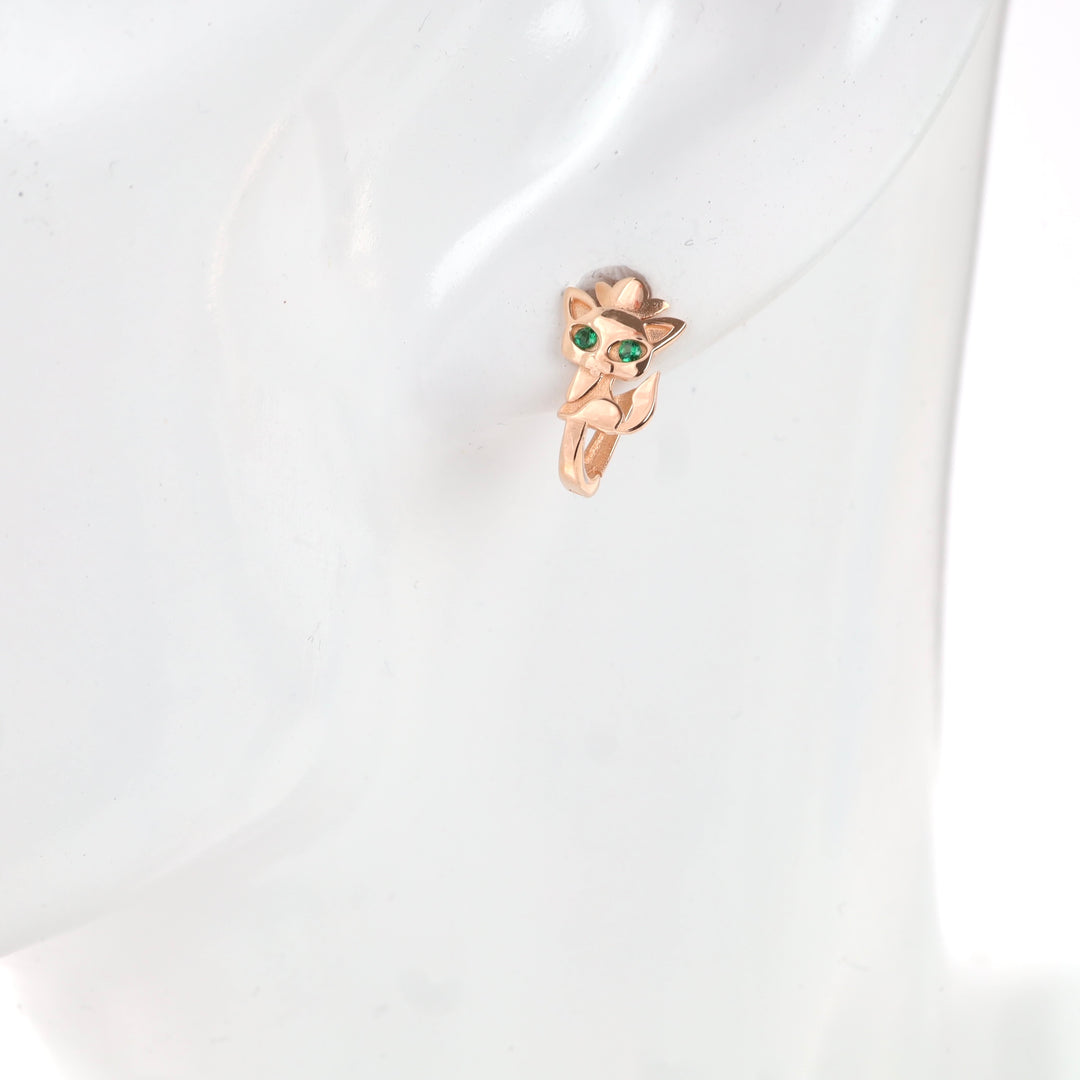 Rose gold cat-shaped earring with green eyes on display stand.