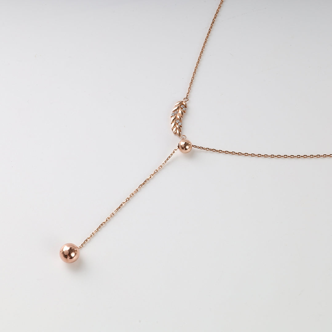Rose gold Y-shaped necklace with a leaf charm and two bead pendants displayed on a white background.