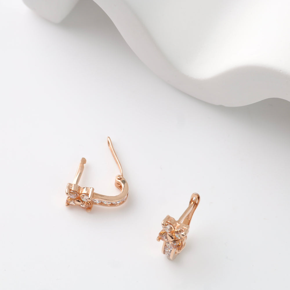 Gold-tone earrings with crystal bow detail on white surface.