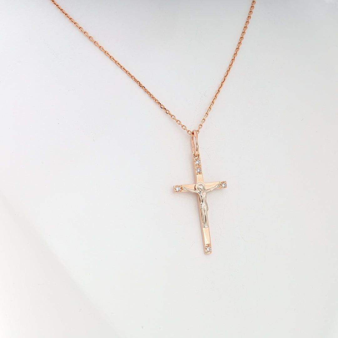 Rose gold crucifix pendant with Jesus figure and small clear stones on a matching chain, shown against a white background.