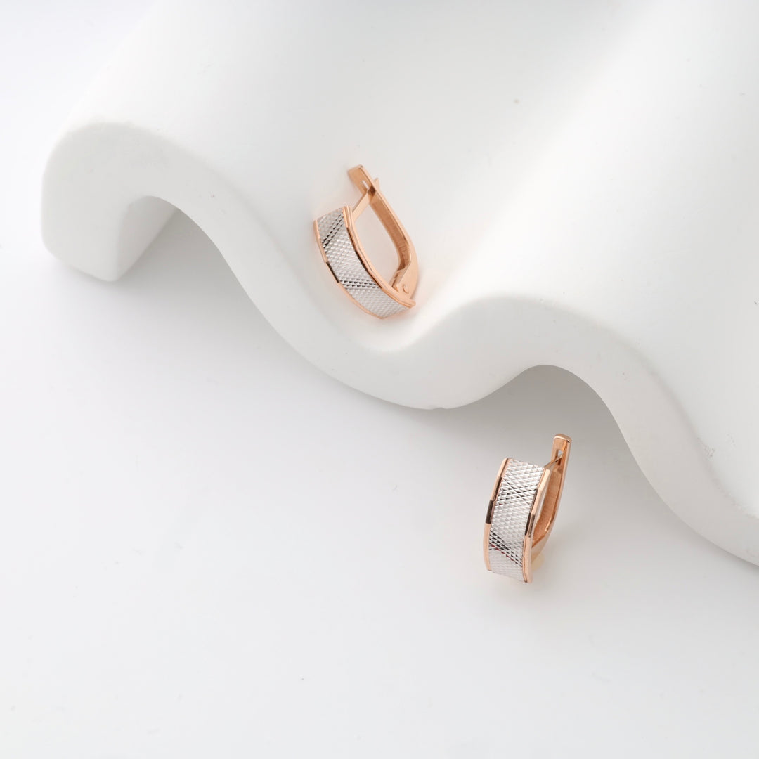 Rose gold-tone huggie earrings with textured silver accent on white background.