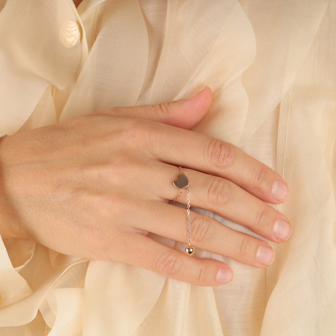 Silver heart chain ring worn on a hand against a cream fabric background, minimalist jewelry, dainty ring.