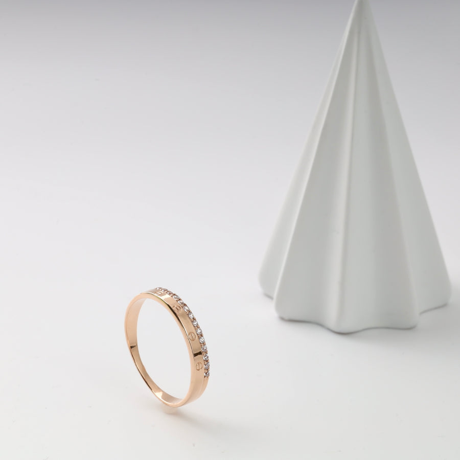 Gold ring with diamonds displayed beside a white cone.