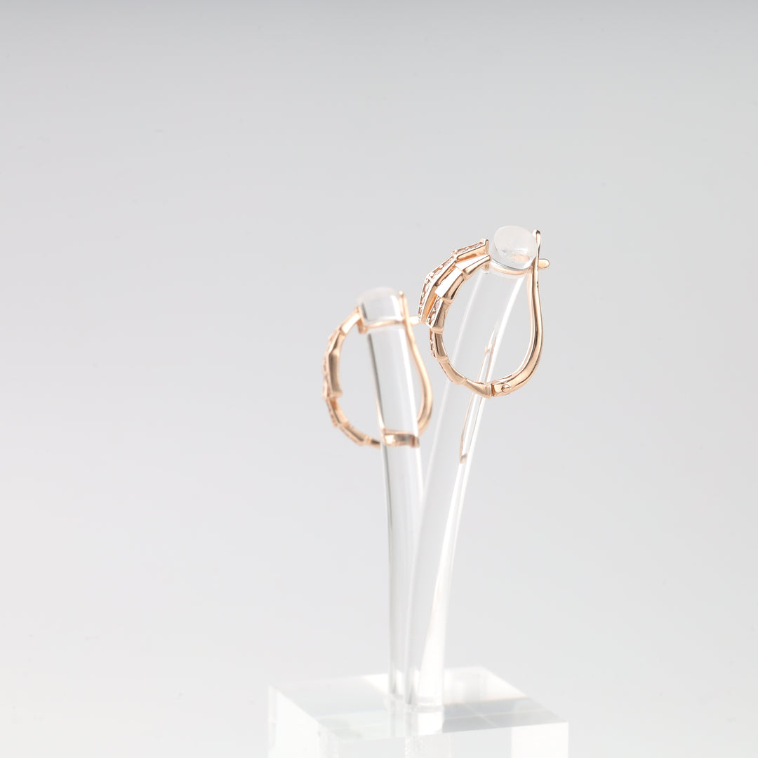 Pair of rose gold hoop earrings with rectangular accents displayed on a clear acrylic stand.