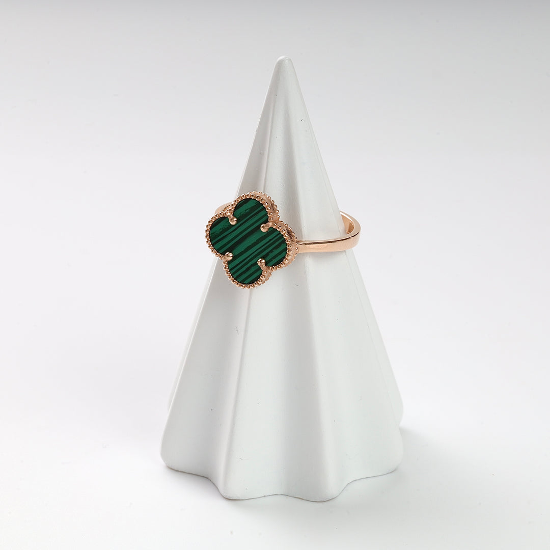 Gold ring with a green malachite clover motif displayed on a white ceramic cone.