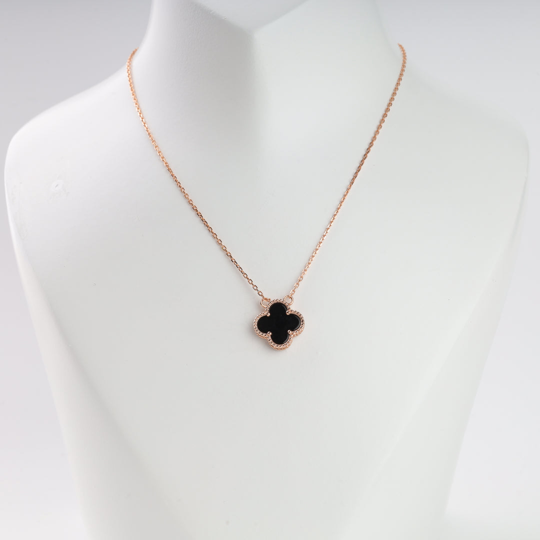 Gold chain necklace with a black four-leaf clover pendant displayed on a white jewelry bust.