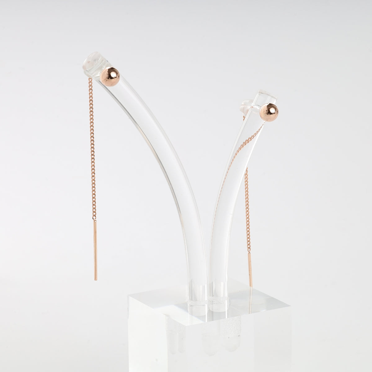 Pair of rose gold threader earrings with fine chain and bar ends, displayed on a clear acrylic stand.
