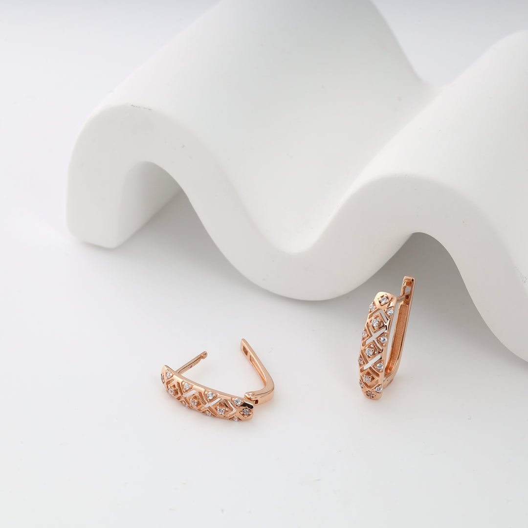 Rose gold diamond huggie earrings with a geometric design on a white decorative background.