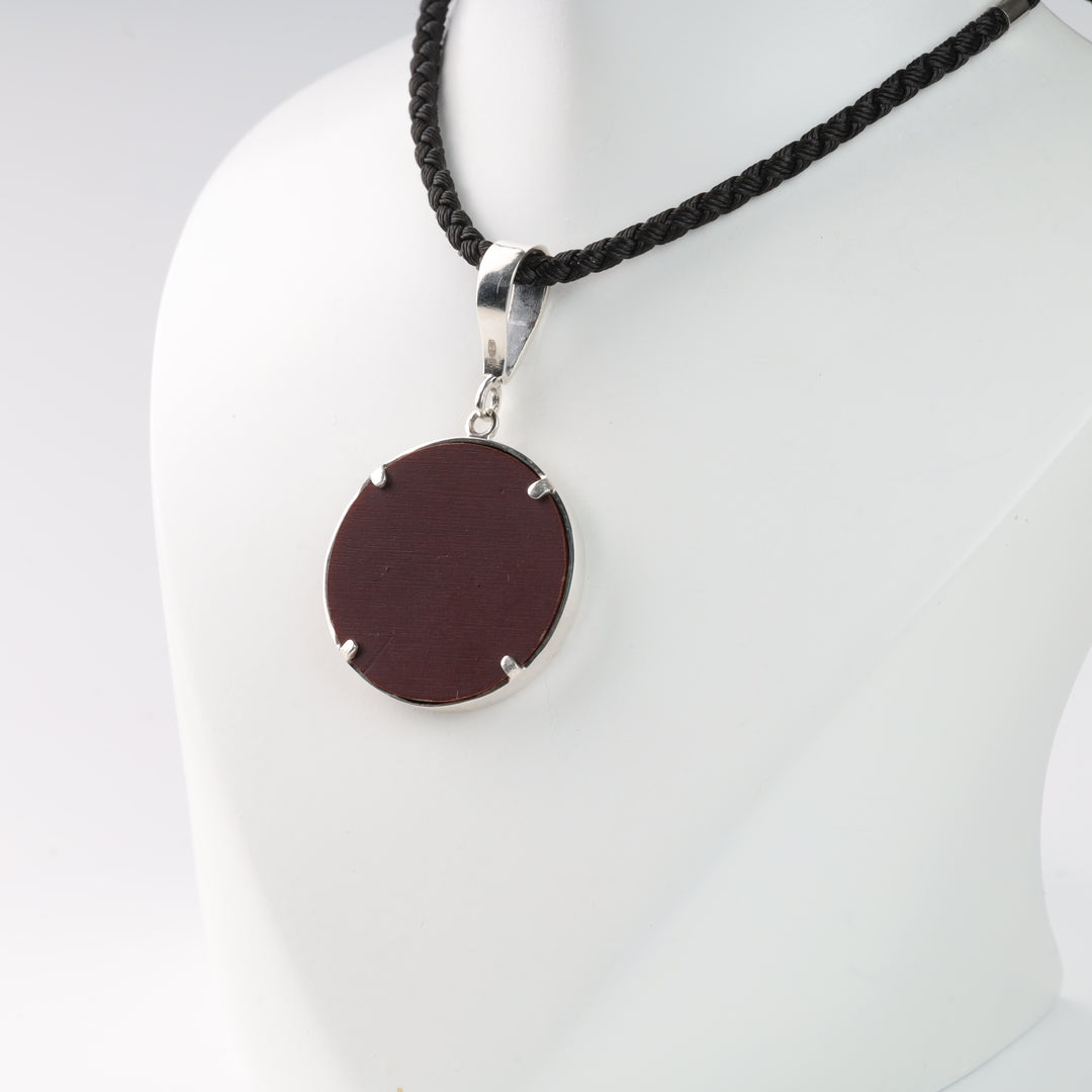 Pendant necklace with a round dark red stone on a black braided cord.
