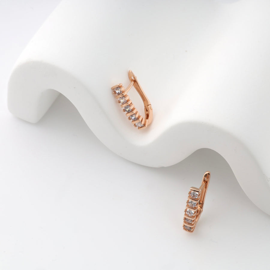 Rose gold hoop earrings with seven small crystals each, displayed on white fabric.