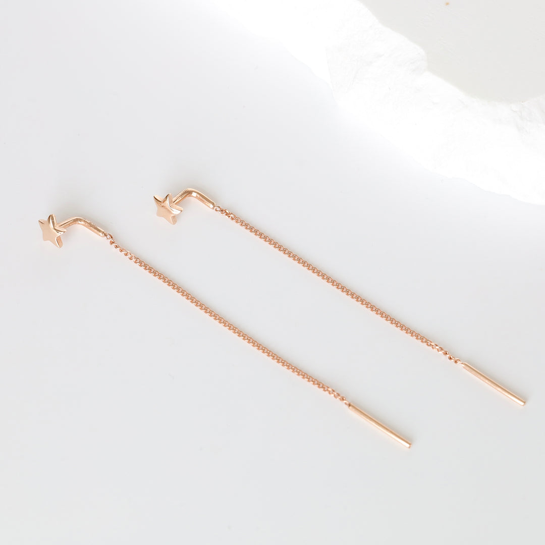 Pair of rose gold threader earrings with star studs and thin bar ends on white background, star stud earrings, chain threader jewelry.
