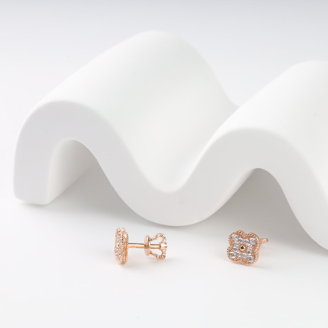 Rose gold stud earrings with floral design and clear gemstones against a wavy white backdrop.
