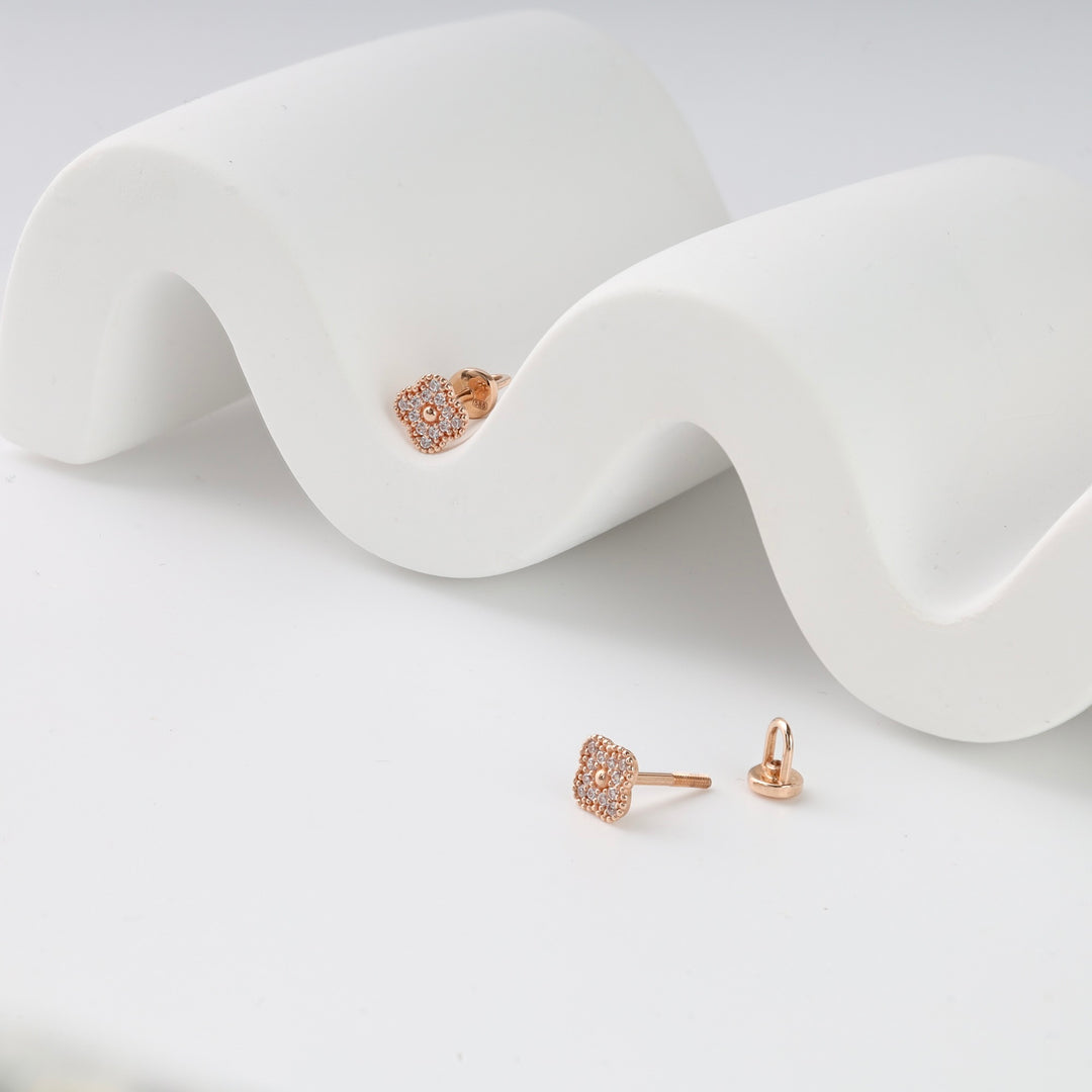 Pair of rose gold floral stud earrings with clear stones, displayed on a white wavy stand.