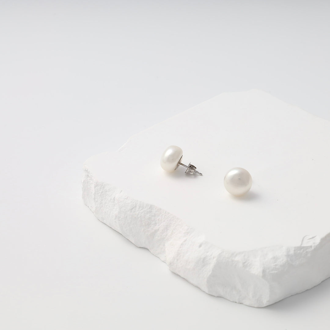 Sterling silver pearl stud earrings on white stone display, classic Ukrainian Jewelry for simple pearl earrings shoppers.