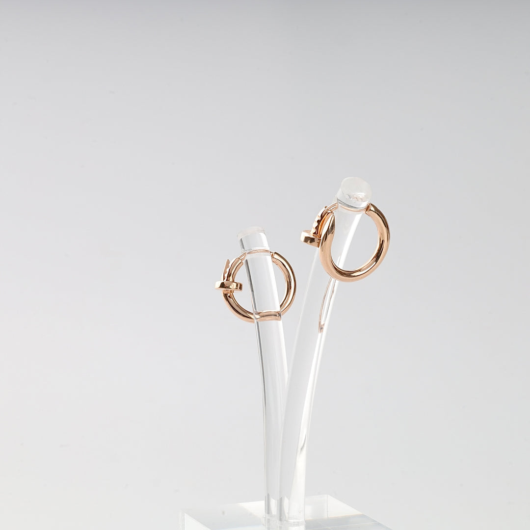 Pair of rose gold hoop earrings displayed on a clear acrylic stand for jewelry photography.