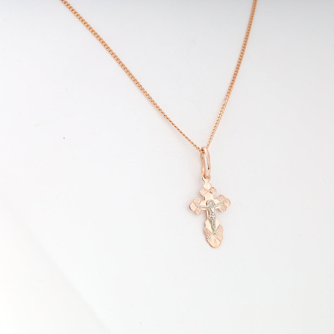 Rose gold chain necklace with a small two-tone crucifix cross pendant shown against a white background.