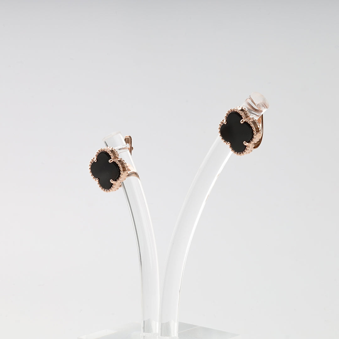 Pair of rose gold clover earrings with black enamel on a transparent stand, quatrefoil stud earrings jewelry.