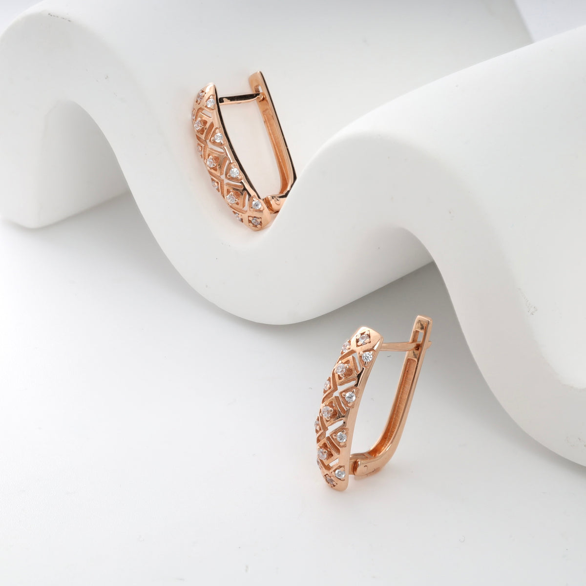 Rose gold diamond huggie earrings with lattice design on white background.