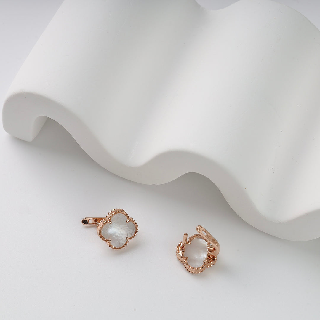 Rose gold hoop earrings with mother of pearl clover charms displayed on a white wavy backdrop.